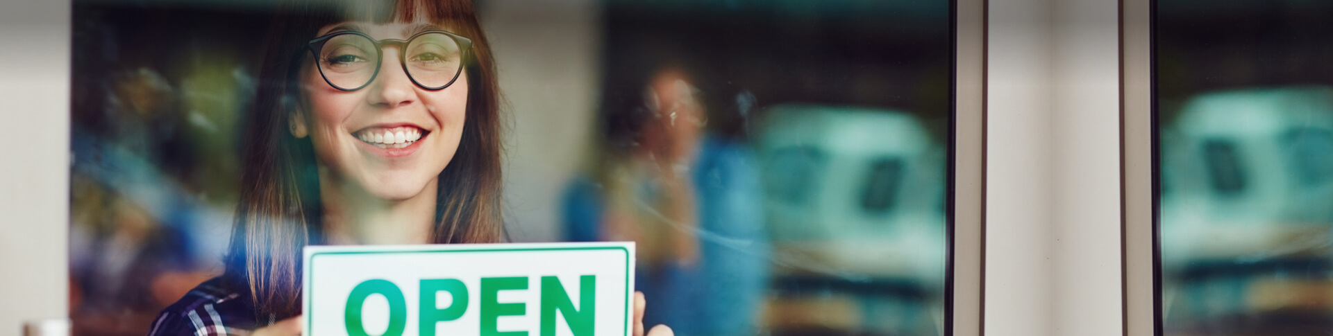 Frau mit Brille hängt Open-Schild in Ladentür