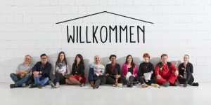 Lächelnde Menschen lehnen an Wand mit Willkommen-Schriftzug