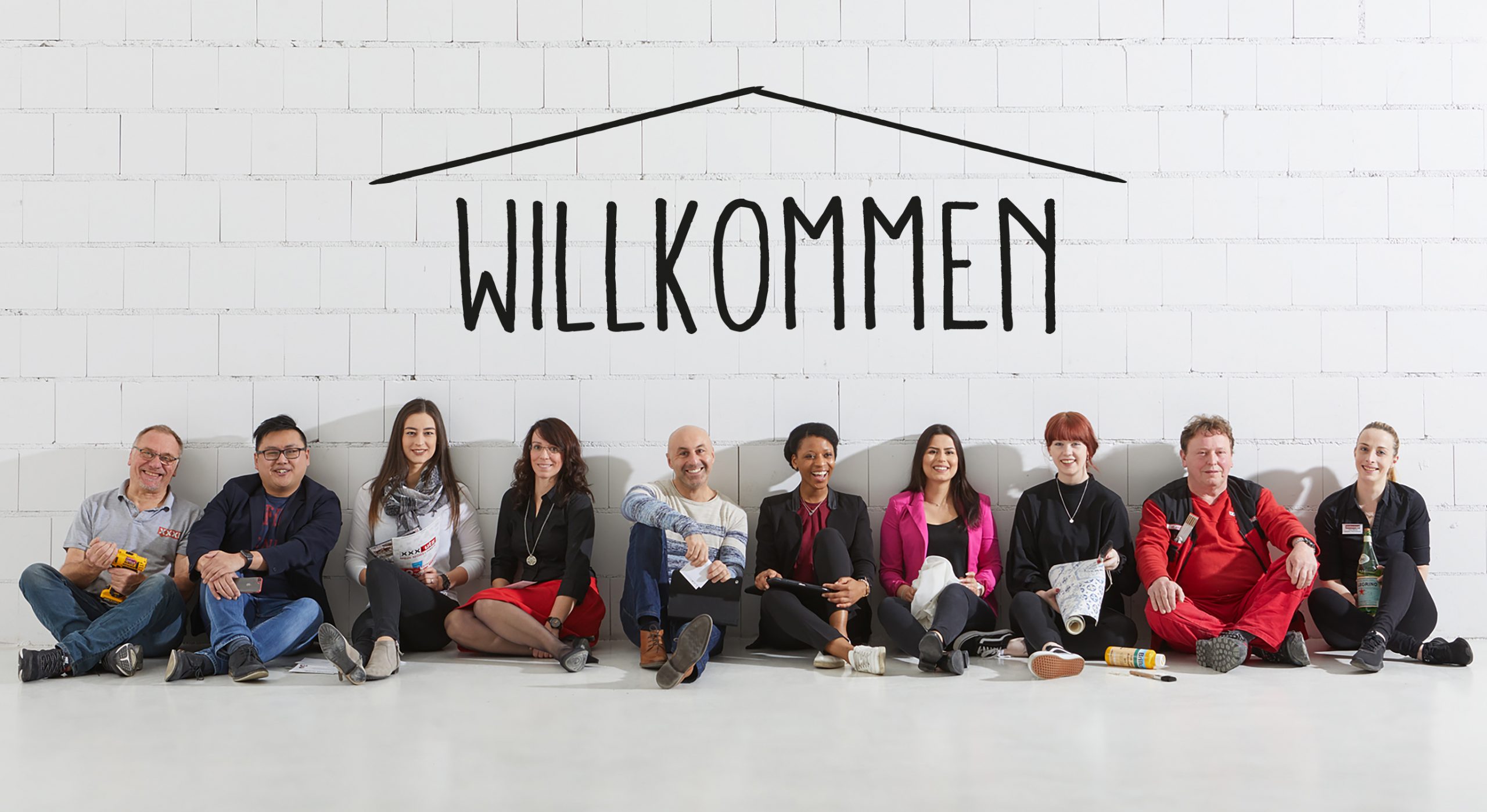 Team vor Ziegelwand mit "Wilkommen" beschriftet