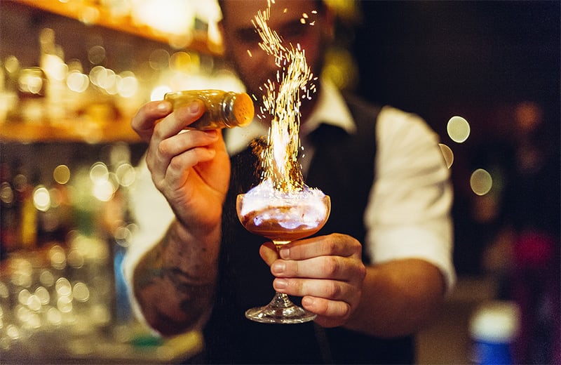Barkeeper würzt flambierten Cocktail